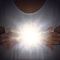 female in white tunic with hands apart at chest level with a bright shining white orb light between