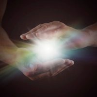 Male hands emerging from darkness, cupped, with rainbow colored bright white star burst of light between